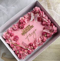 a pink birthday cake in a box with flowers on the side and a name written on it