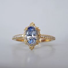 an oval shaped blue and white diamond ring on a white surface with the center stone surrounded by smaller round diamonds