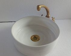 a white sink with a gold faucet on the side and a wall behind it