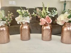 four vases with flowers in them sitting on a white table next to a couch