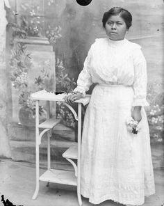 an old photo of a woman standing next to a table