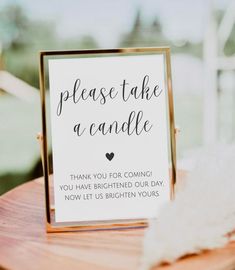 a sign that says please take a candle on top of a wooden table with feathers