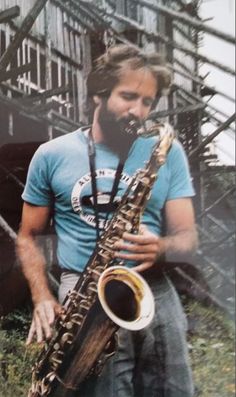 a man with long hair and beard playing a saxophone in front of a staircase case