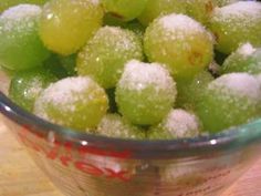 a bowl filled with green grapes covered in powdered sugar on top of a wooden table