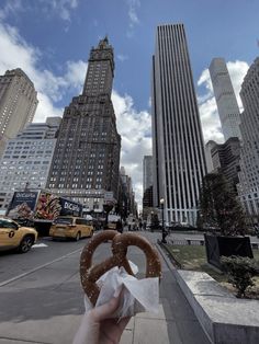 a person holding up a pretzel in the middle of a city with tall buildings