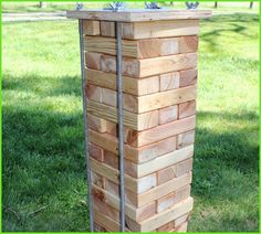 a wooden tower made out of wood blocks in the grass with a hose attached to it