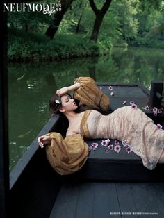 a woman laying on the back of a boat in a body of water next to trees