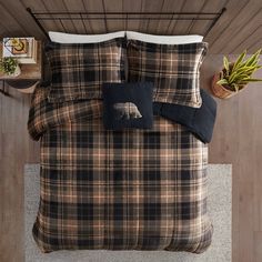 a bed with plaid comforter and pillows in a room next to a potted plant