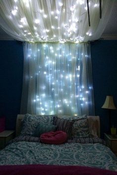 a bed with lights hanging from the ceiling in front of a curtained window over it