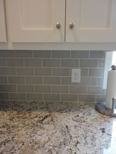 a granite counter top in a kitchen with white cabinets and gray tile backsplash