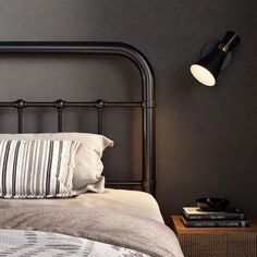 a black metal headboard with two pillows and a lamp on the wall above it