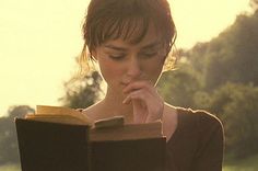 a woman is reading a book in the grass with her hands on her face and looking down