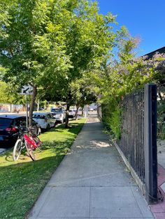 a bike parked on the side of a sidewalk next to a tree and fenced in area