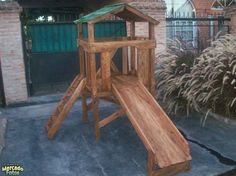 a wooden play set with a green roof and slide in front of a brick building