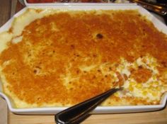 a casserole dish with cheese and meat in it on a wooden table next to utensils