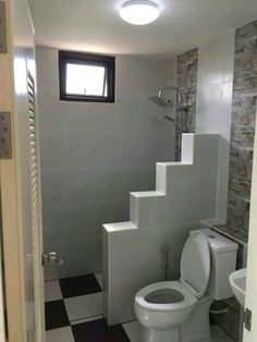 a white toilet sitting under a window next to a sink in a room with tiled walls