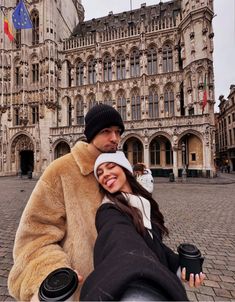 a man and woman taking a selfie in front of an old building with flags on it