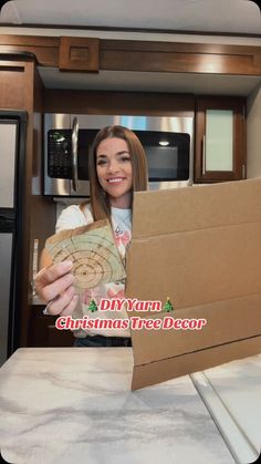 a woman holding a cardboard box in her hand and smiling at the camera while standing next to an oven