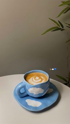 a cup of coffee on a saucer with clouds painted on the foam in front of it