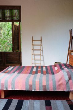 a bed sitting in a bedroom next to a window with a ladder on top of it