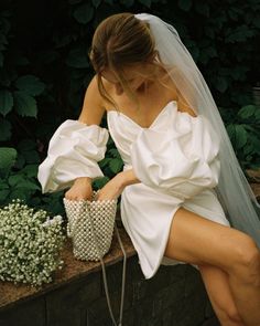 a woman in a white dress is sitting on a brick wall with her legs crossed