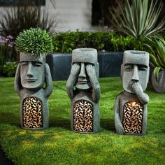 three stone statues with plants growing out of their heads on the grass in front of some bushes