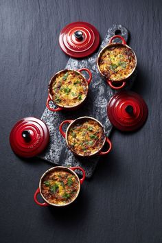 four red pots filled with food sitting on top of a black tablecloth next to each other