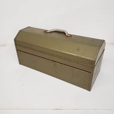 an old metal box is sitting on the floor next to a white wall with a silver handle