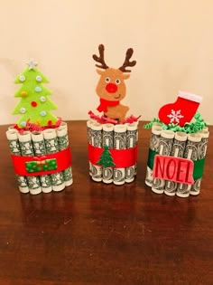 three christmas decorations made out of rolled up money on top of a wooden table next to a wall