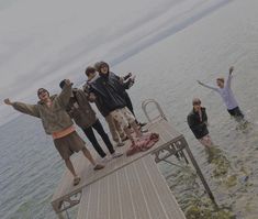 a group of people standing on top of a wooden pier next to the ocean with their arms in the air