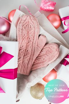 a pair of pink knitted mittens sitting in a box surrounded by balloons and streamers