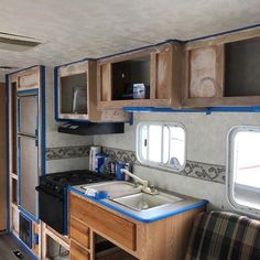 the interior of an rv with wood cabinets and blue trim around the windows, sink and stove