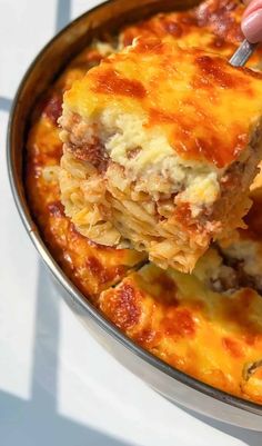 a person holding a fork in a casserole dish with meat and cheese on it