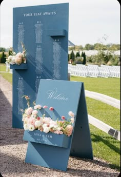 a blue sign with flowers on it sitting in the grass