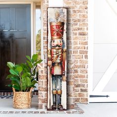 a wooden nutcracker is on the front porch next to a potted plant