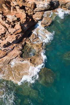 two people are standing on the rocks by the water's edge looking out at the ocean