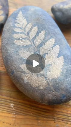 a rock with leaves painted on it sitting on top of a wooden table next to other rocks