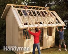 two men are building a small house with windows and sidings on the roof, while another man is standing in front of it