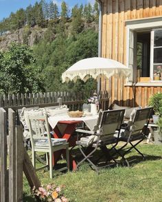 an outdoor table and chairs with an umbrella in the grass next to a wooden fence