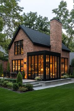 a brick house with large windows and lots of greenery in the front yard at night