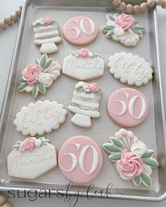 decorated cookies with pink and white frosting are on a cookie sheet that says happy 50th