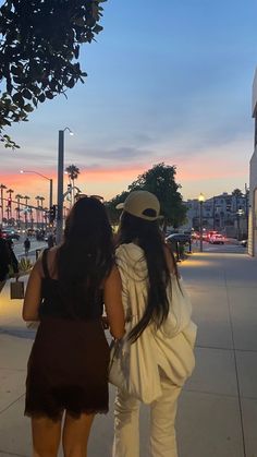 two women are walking down the sidewalk at sunset or dawn with their backs to each other