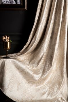 a gold vase sitting on top of a wooden table next to a white drapes