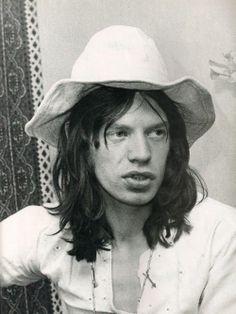 a man with long hair wearing a white hat and posing for a photo in front of a curtain