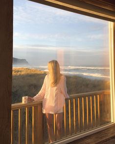 a woman standing on a balcony looking out the window at the ocean and sand dunes