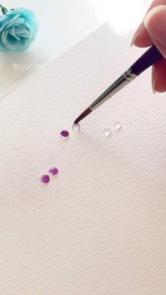 a person is holding a pen and writing on paper with three small purple stones in front of them