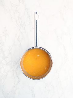 an orange sauce in a metal bowl on a marble counter top with a silver spoon