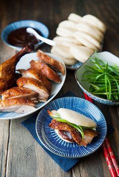 a table topped with plates and bowls filled with meat covered in sauce next to veggies