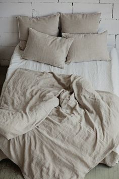 an unmade bed with linens and pillows on it in front of a white brick wall