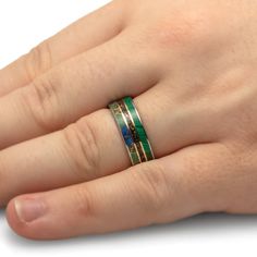 a person's hand with a ring on top of their finger, wearing a green and gold band